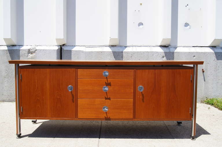 This Finn Juhl credenza, constructed of teak with aluminum accents, features a floating case with three drawers and two enclosed shelving areas.