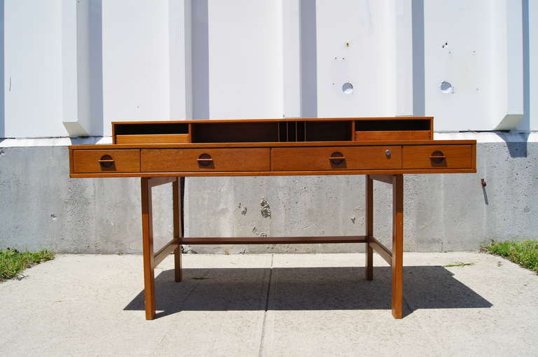 This desk was designed by Peter Lovig Nielsen. It features four drawers with unique tab drawer pulls, one of which has a working lock. The upper storage portion features two drawers and open storage for papers. This portion can flip down, converting