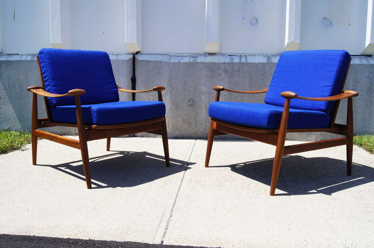 This pair of armchairs was designed by Finn Juhl and manufactured by France & Daverkosen. They feature a teak frame with elegantly curved arms and foam cushion seats.