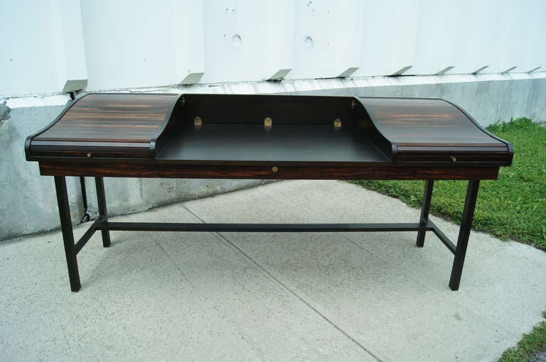 This desk was designed in 1957 by Edward Wormley for Dunbar. It features two rosewood roll-top doors that each conceal two small drawers, as well as three shallow drawers below. The desk also has a hinged panel that allows it to convert to a