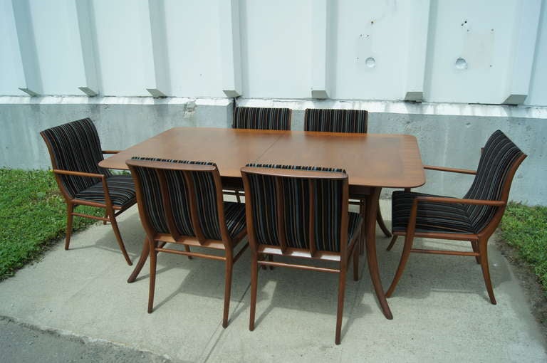 Designed by T.H. Robsjohn-Gibbings for Widdicomb, this elegant set features a large, saber-leg dining table and six saber-leg chairs (two armchairs and four side chairs) in mahogany. 

The table has two leaves, each measuring 18" wide, which