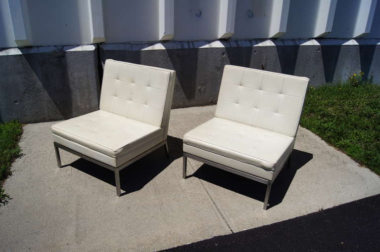 This pair of lounge chairs by Florence Knoll feature brushed chrome bases with tufted white vinyl upholstery.