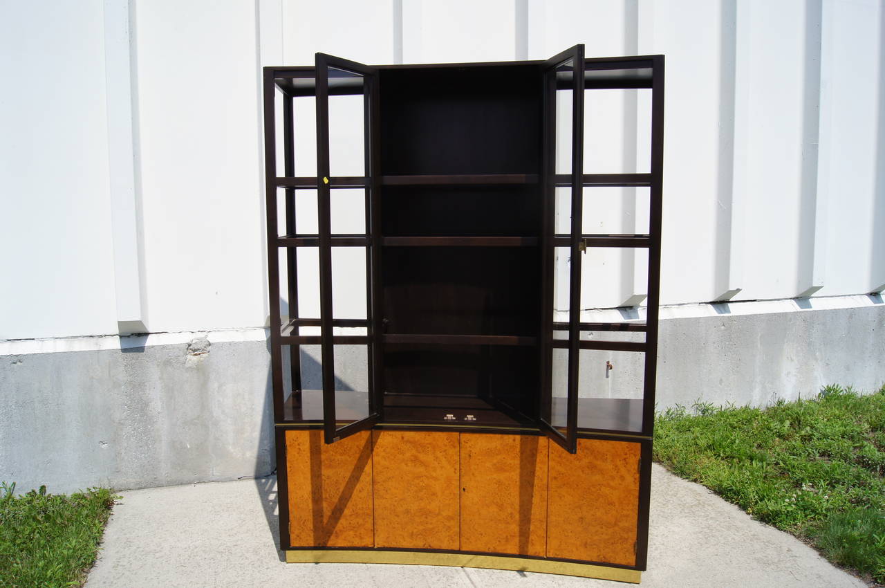 Edward Wormley designed this elegant display cabinet, model #6027, for Dunbar. The olive burl doors of the lower case enclose shelving and a segmented drawer. The ebonized walnut frame above holds six open glass shelves and more shelving behind