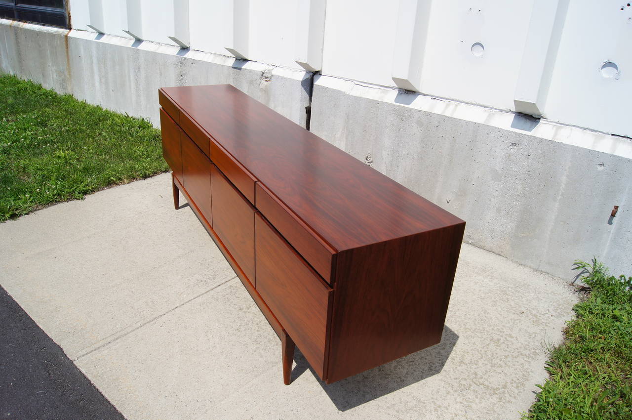 Designed by Ib Kofod-Larsen and manufactured in Denmark in the 1960s, this clean-lined sideboard features beautifully grained rosewood. The case sits on a raised base and offers four drawers above a four-door cabinet section with open storage and