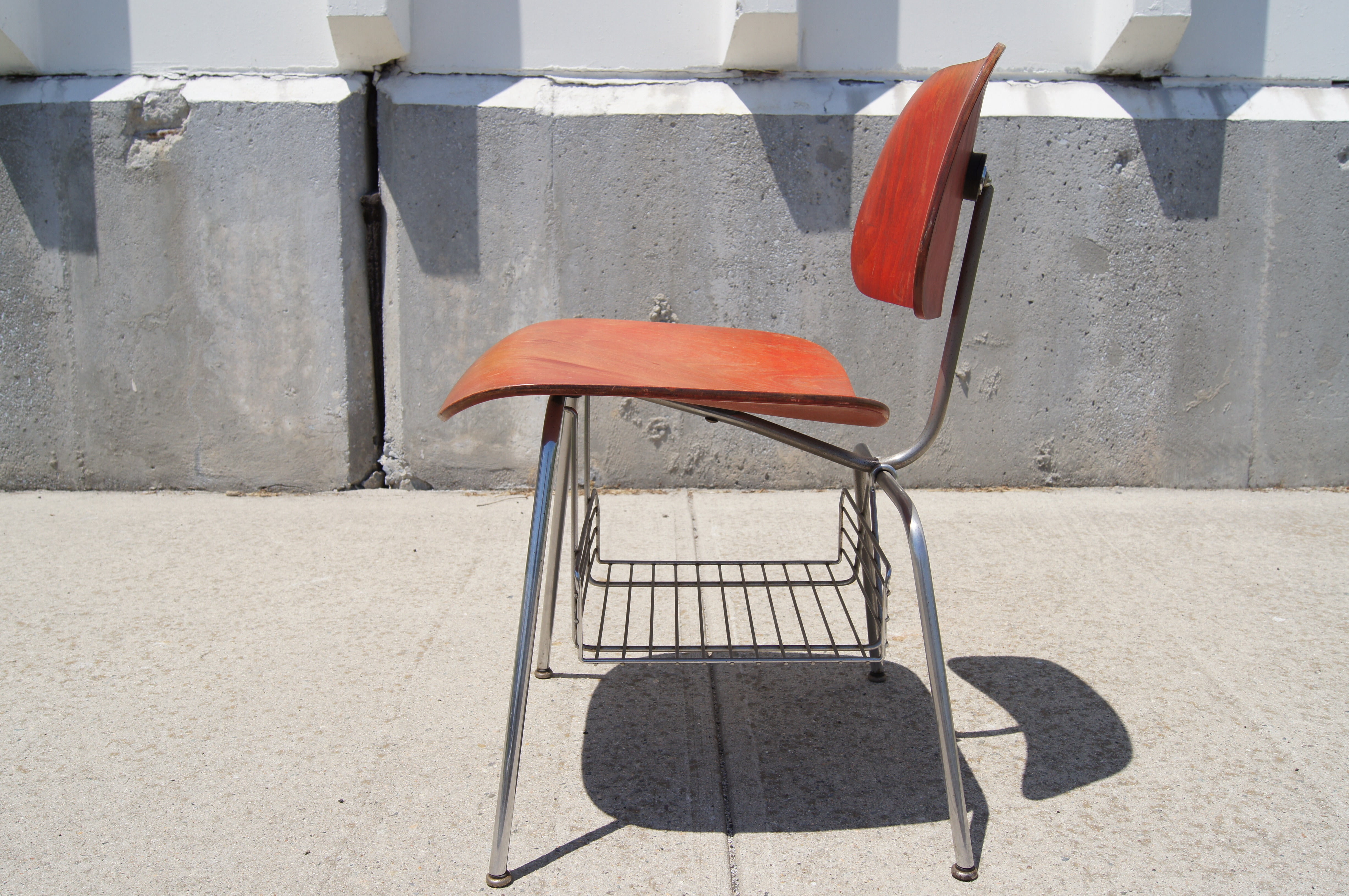 This rare iteration of the Eames's DCM side chair, produced by Herman Miller between 1950 and 1954, features a chrome wire magazine rack below the seat. The bent plywood is finished in aniline red. 

Original Herman Miller foil strip label.