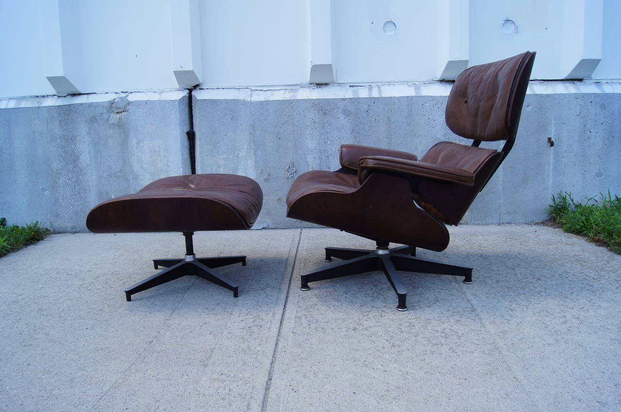 This is an early example of the iconic lounge chair and ottoman designed by Charles & Ray Eames for Herman Miller. An item for collectors of original condition pieces, it features patinated rosewood veneer, brown leather and down filling.