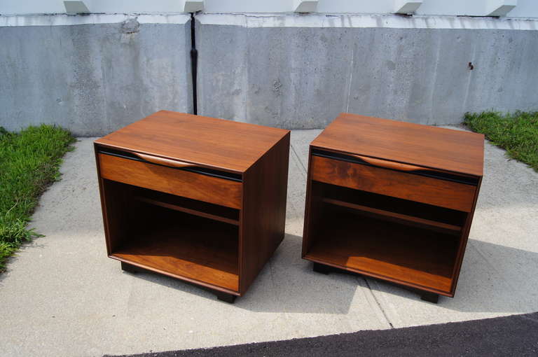 This pair of walnut nightstands was designed by John Kapel and manufactured by John Stuart Inc. Each nightstand features one drawer and open storage with a recessed shelf. 

Corresponding tall chest and dresser also available.