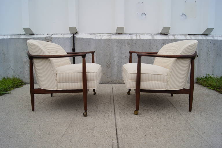 These armchairs, designed by Ib Kofod-Larsen, feature open walnut frames and newly upholstered off-white striped seats. Each chair has two casters to facilitate mobility.