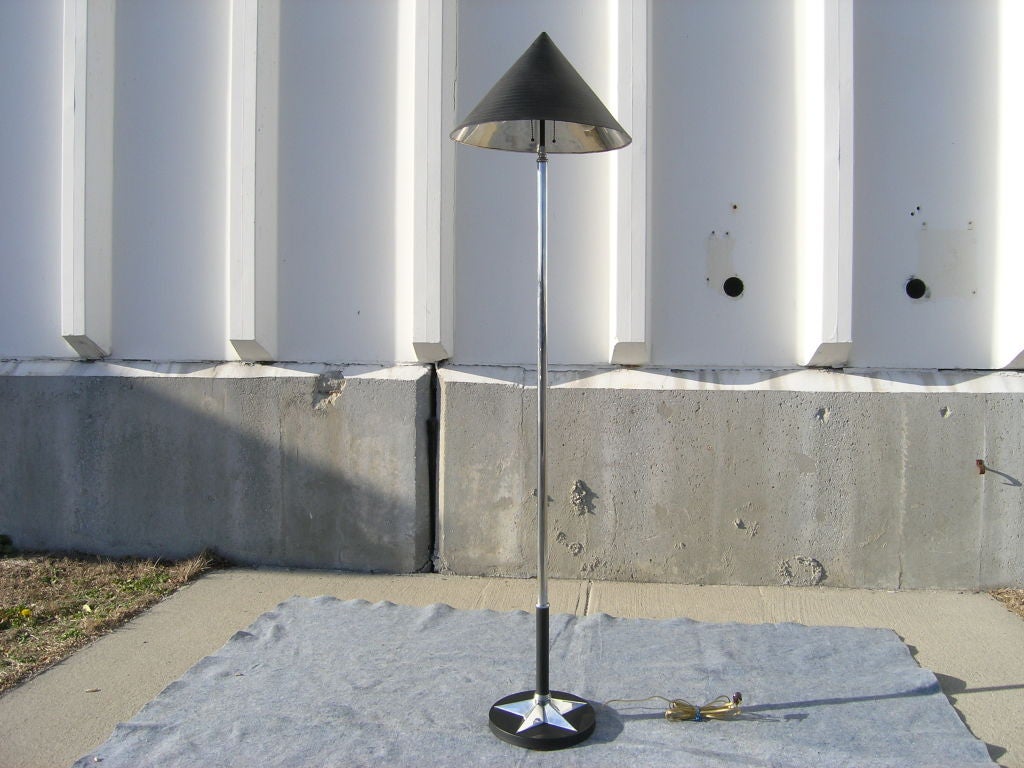 This streamlined Art Deco floor lamp from the 1930s contrasts polished aluminium with matte black enamel. Black on the exterior, the conical shade's reflective interior casts a beautiful glow. The slender stem rises from a bold shiny star set on a