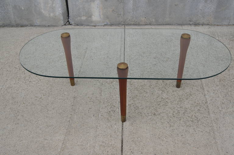 Unique three-legged coffee table with glass racetrack top and brass-capped legs.