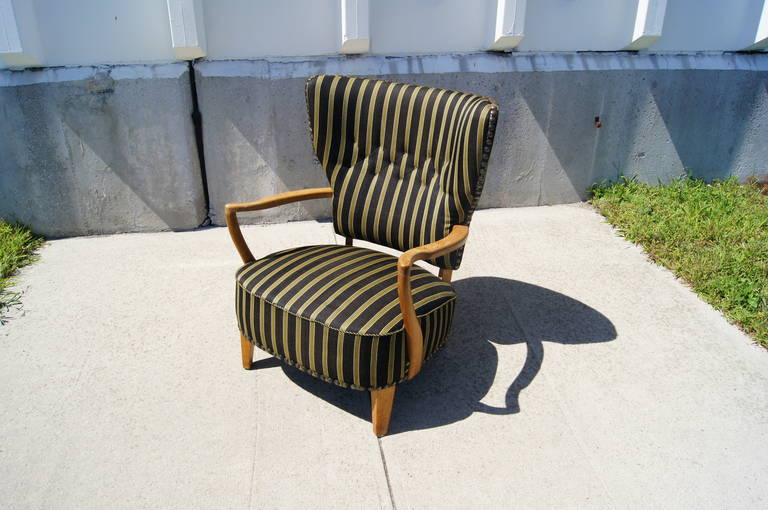 This wonderful highback lounge chair was designed in Sweden in the 1950s. Carved oak arms and legs contrast with the substantial seat and exuberant back, which are upholstered in a striped black and green textile with metal rivets and rope piping.