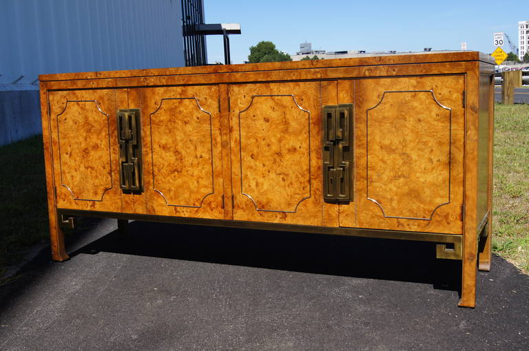 Mastercraft constructed this stunning sideboard, attributed to William Doezema. The honey-toned amboyna burl wood case features four brass-welted doors accented by large brass chinoiserie pulls. The doors conceal a drawer and an adjustable shelf on