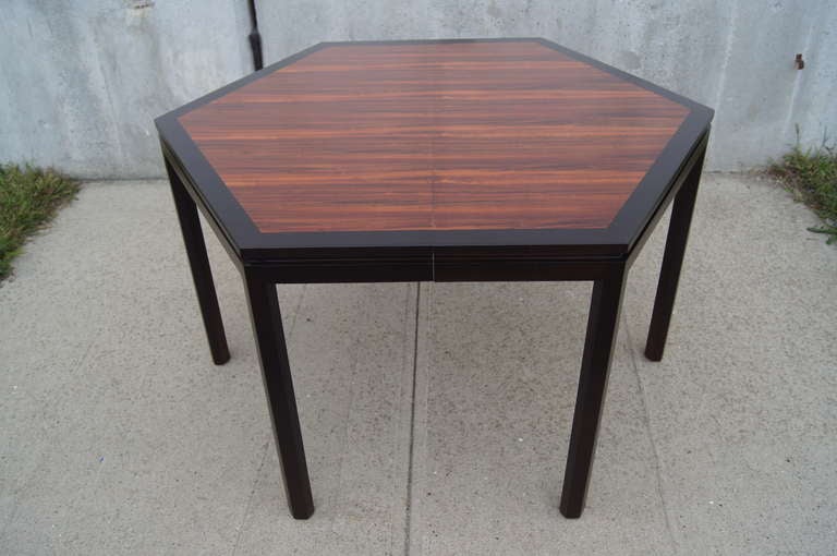 Designed by Edward Wormley for Dunbar, this striking dining table comprises a rosewood top boldly edged with ebonized mahogany that extends to the legs. Two 16-inch leaves allow the hexagonal shape to be stretched to 83.75 inches from point to point.