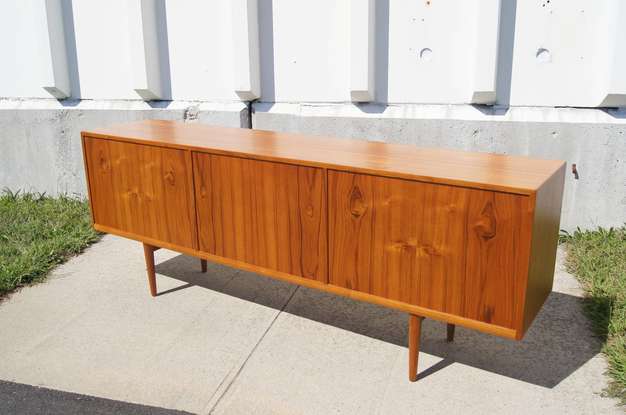 This sideboard is constructed of teak and features two cabinet storage sections with adjustable shelving and four felt-lined drawers.