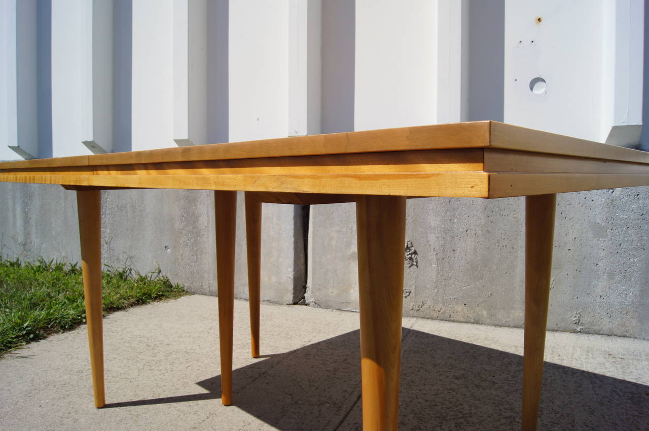Dieser vielseitige moderne amerikanische Esstisch wurde von Russel Wright für Conant Ball entworfen. Er ist aus massivem Ahornholz gefertigt und hat drei 11::25-Zoll-Blätter:: die zusammen eine Tischplatte von 96 Zoll ergeben. Die sechs Beine des
