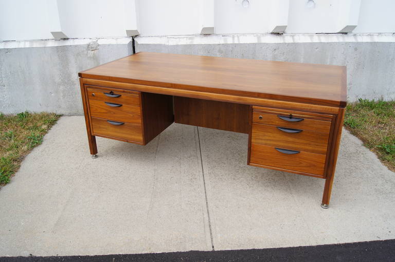 Designed by Jens Risom in the 1960s, this handsome executive desk can also serve as a partners' desk. Constructed of richly grained solid walnut, it has two pull-out writing surfaces above two sets of three drawers that feature black demilune