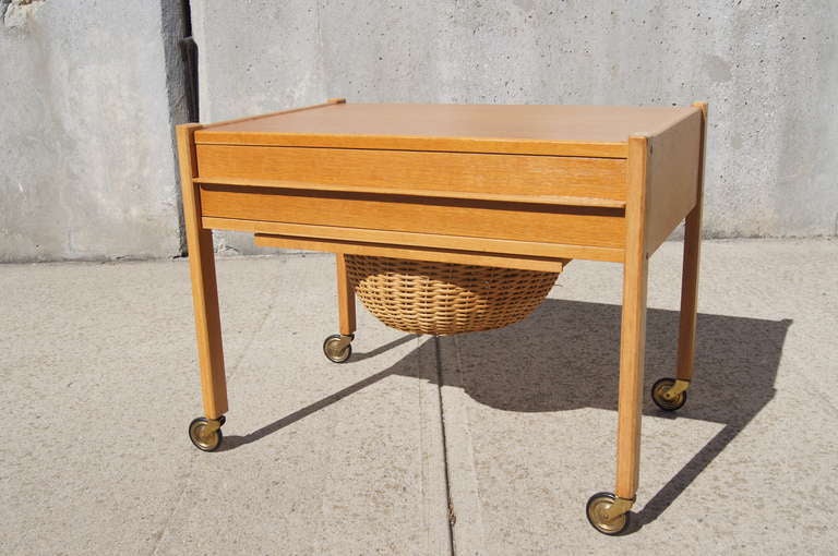 For the home sewer, knitter, or weaver, this mid-century Danish sewing cart offers clean-lined style. Constructed of a warm oak frame with legs on brass casters, it features a slide-out wicker basket below a shallow partitioned drawer.