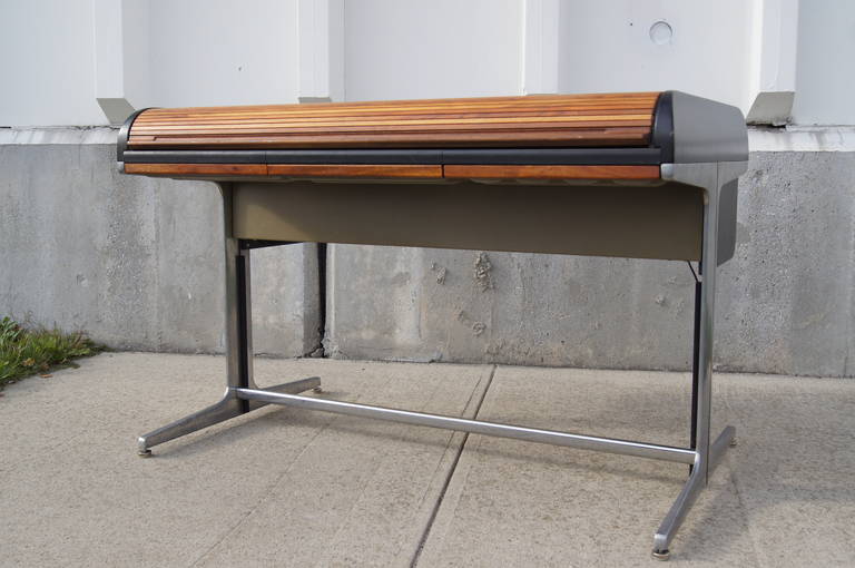 This Action Office desk by George Nelson for Herman Miller features a walnut roll-top over a laminate desk surface and aluminum frame, four shallow wood-front drawers, painted sides, and metal dividers for files at the back of desk surface. It is
