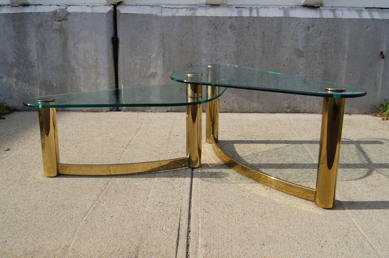 This 1970s coffee table by Pace collection comprises two overlapping glass triangles set on brass columns that rise from a curvilinear base, creating a dynamic view from every angle. 

The lower glass top is 14 inches high, while the upper is