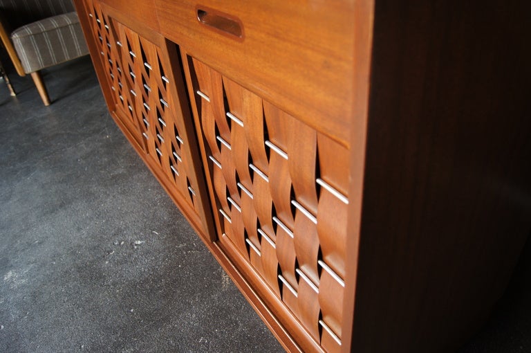 Designed by Edward Wormley for Dunbar, this handsome sideboard features sliding doors whose mahogany veneer strips are interwoven with nickel rods. The doors open to reveal three storage areas: The center section has two adjustable shelves, and the