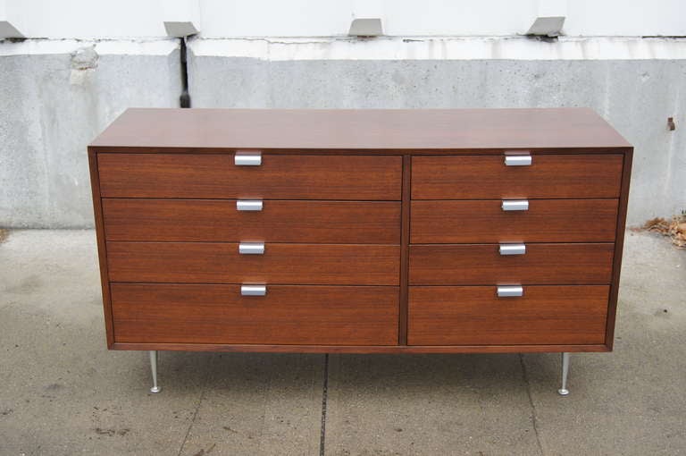 Designed by George Nelson for Herman Miller, this walnut dresser features satin chrome J-shaped drawer pulls and rare tapered satin chrome legs. Four of the eight drawers are slightly larger than the others, giving the dresser an attractive
