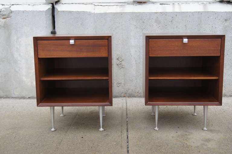 This pair of night tables, designed by George Nelson for Herman Miller, is constructed of walnut and features satin chrome J-shaped drawer pulls and rare satin chrome tapered legs. Each nightstand features one drawer above an open storage area with