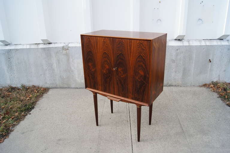 This rosewood bar by Illum Wikkelsø has two doors that open to reveal a diamond-patterned mirrored bar with one glass shelf. Each door has four slots for storing bottles. Below the cabinet there is a pull-out shelf the provides a surface for pouring