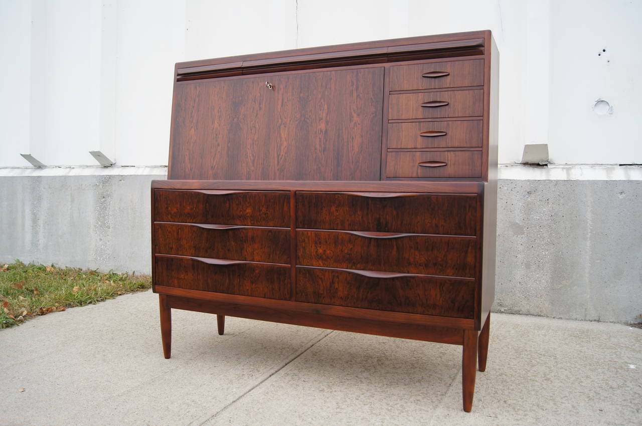 This secretaire desk was designed by Ib Kofod-Larsen and manufactured in Denmark. It features six large bottom drawers, four smaller drawers, and a locked secretaire cabinet that houses additional storage and provides access to hidden storage.