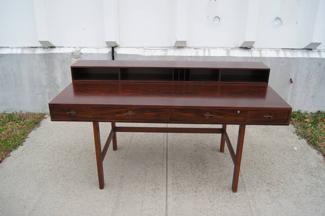 This desk was designed by Peter Løvig Nielsen. It features four drawers with unique tab drawer pulls, one of which has a working lock. The upper storage portion features two drawers and open storage for papers. This portion can flip down, converting