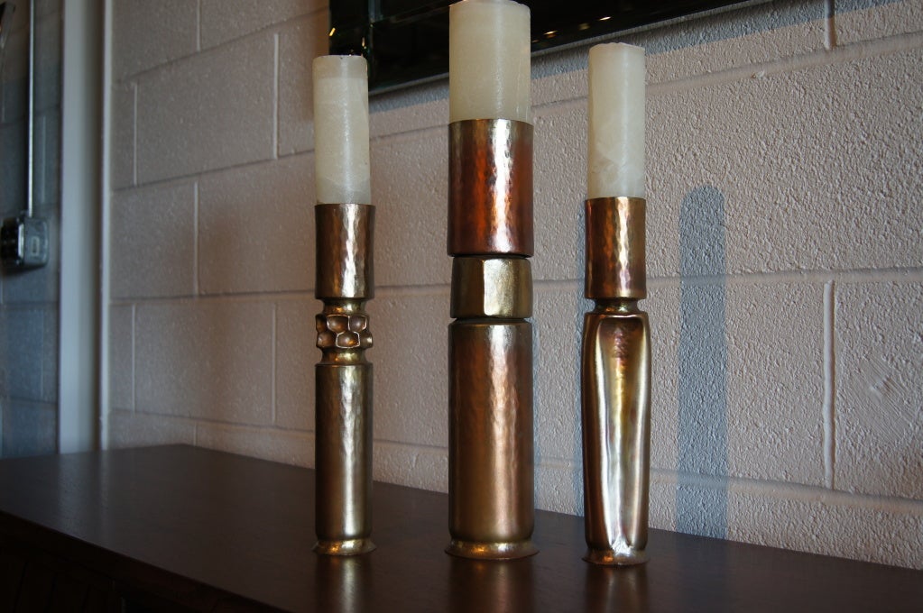 Metalsmith Thomas Roy Markusen forged this set of three complementary copper candlesticks in the 1970s. They have been heat oxidized to create a richly colored patina. 

The two smaller candlesticks measure 12.5 inches in height and 2.25 inches in