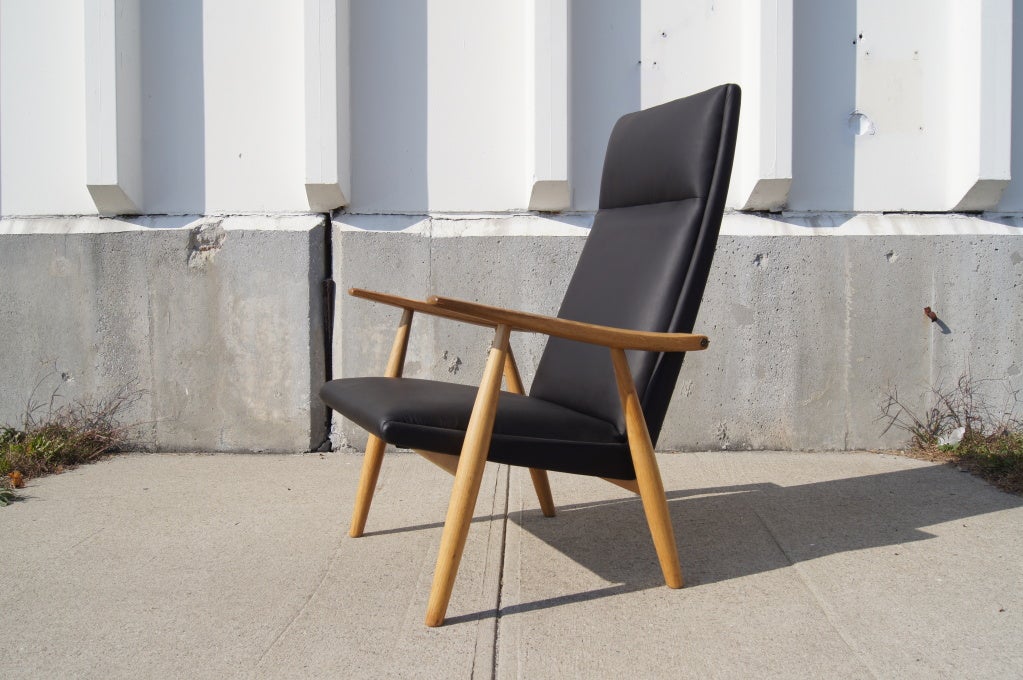 Hans Wegner entwarf diesen minimalistischen Sessel, Modell GE-260A, 1950 für GETAMA. Das Gestell aus massivem Eichenholz trägt eine markante hohe Rückenlehne, an der die konisch zulaufenden Arme mit Messingbeschlägen befestigt sind. Das Federsystem