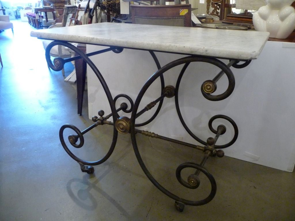 An iron, brass and marble-top bakers table with a scrolled base and a wonderful patina.