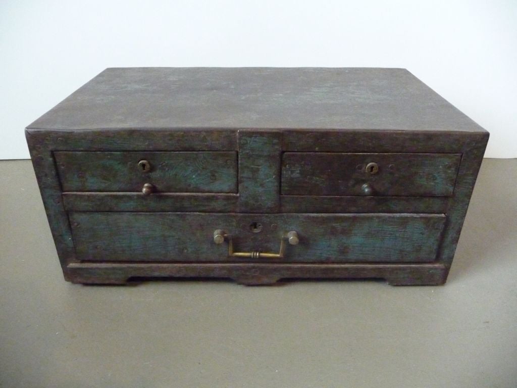A three-drawer coffer or strong box with a worn turquoise patina on a footed base.
