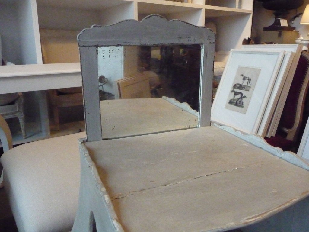 Wonderful vanity with a pull-up mirror that can be lowered to be hidden. Serves as a vanity, side table or nightstand. One-drawer, grey paint. Circular cut-outs on both sides with carved decorative edges.