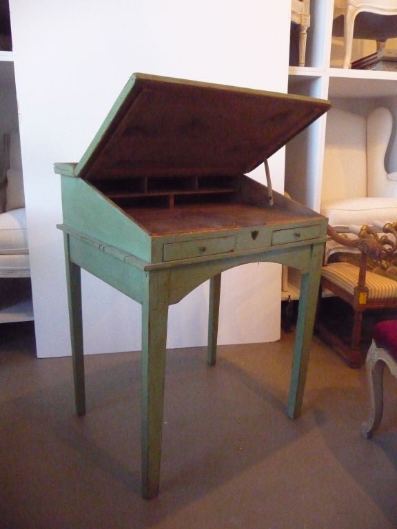 Slant top green painted pine scribes desk. The desk opens to an adjustable height and has multiple drawers and shelves for storage, including a lift-up compartment hidden in the desk.