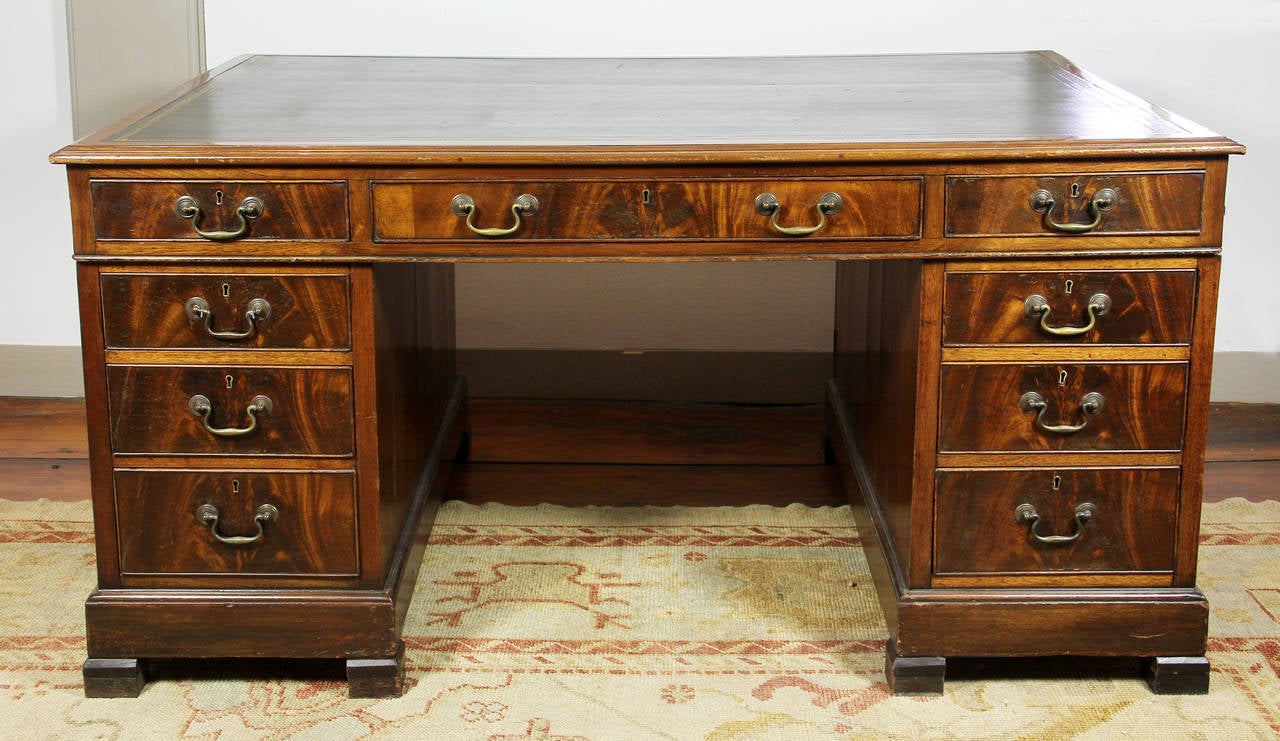 Rectangular tooled leather top over a long drawer flanked by two short drawers with opposing identical configuration, bases with three drawers with opposing cabinet doors, bracket feet.