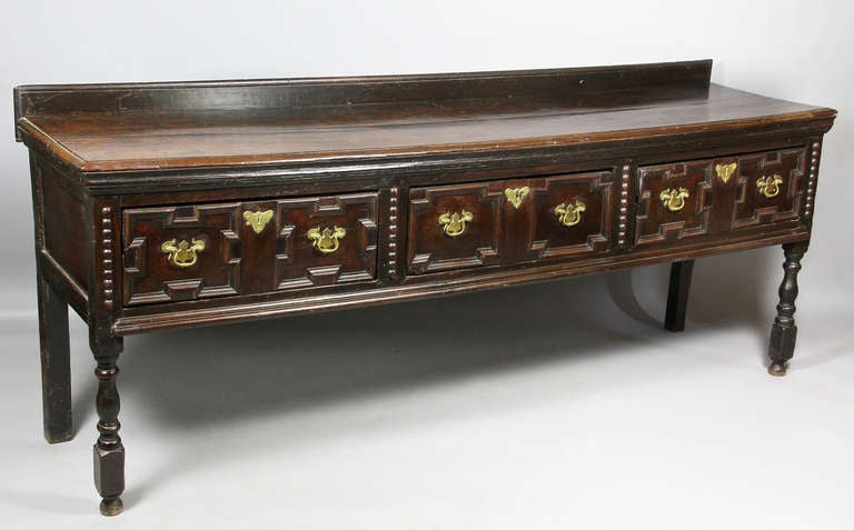 Rectangular top with 3.25 inch low back board over three panelled drawers with alternating beaded dividers raised on turned legs.