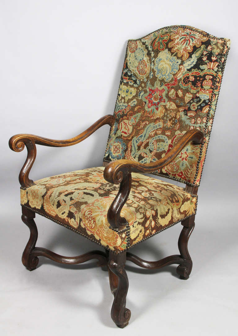 Arched back and square seat, scrolled arms, os de mouton legs with shaped x stretcher. Needlepoint with brass tacks.