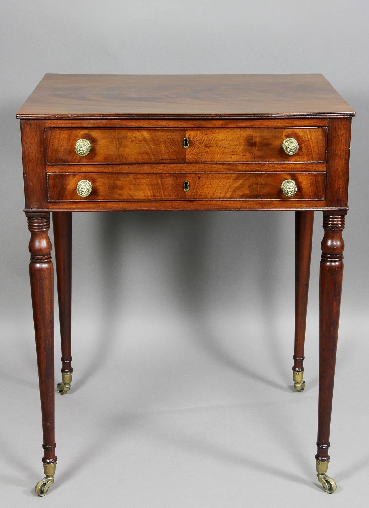 Wonderfully figured rectangular top over two drawers, raised on turned tapered legs, casters.