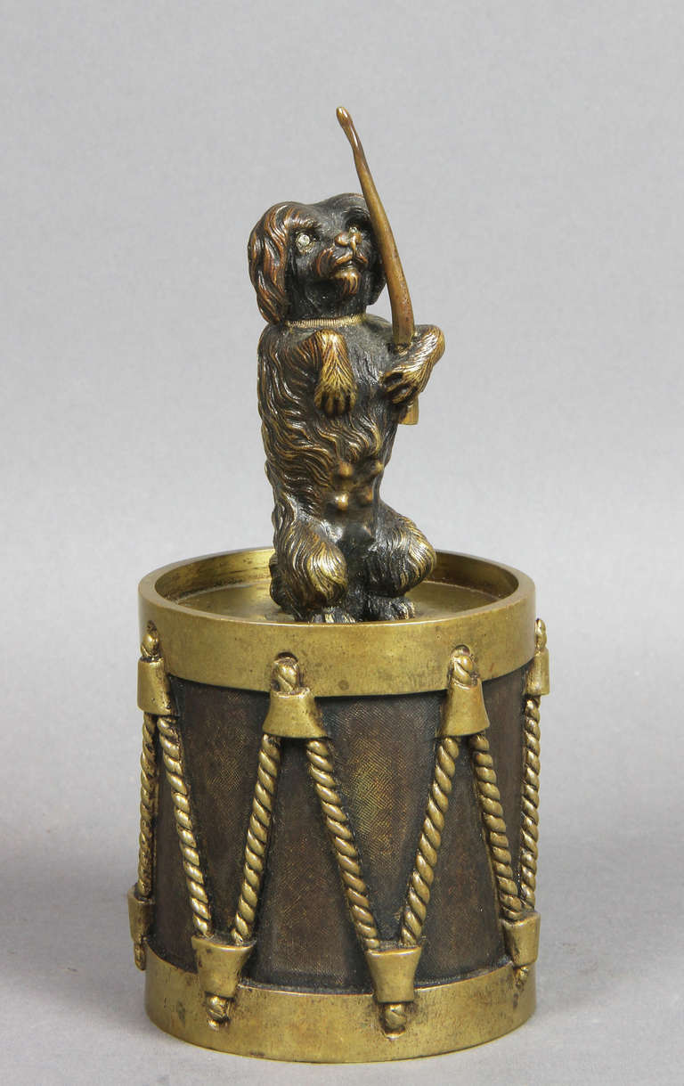 Dog with cut-glass eyes holding a drum stick and seated on a drum.