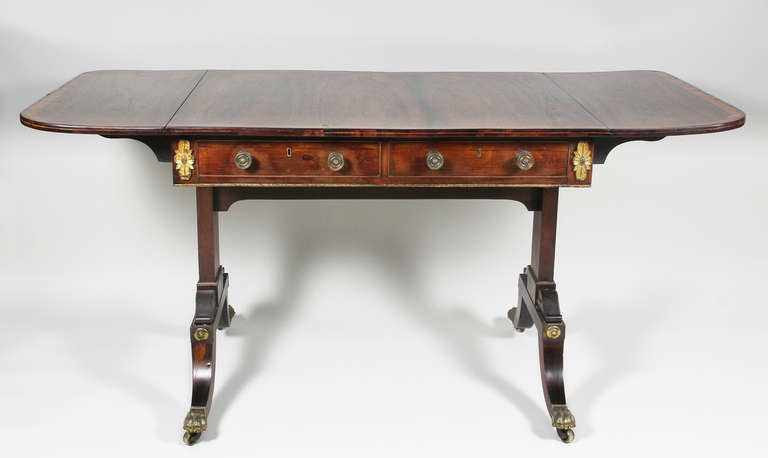 Rectangular satinwood crossbanded top with hinged end leaves above a pair of drawers with opposing false drawers , trestle base with gilt bronze volutes over saber legs , casters.