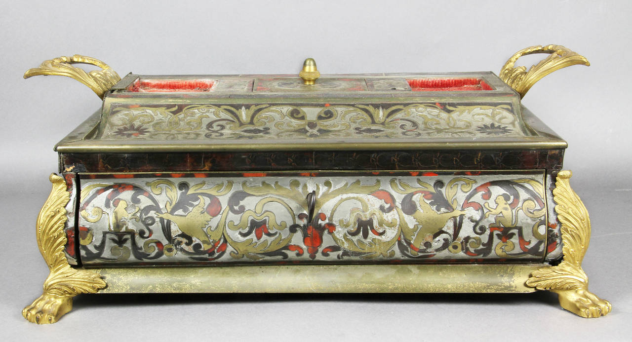 Rectangular with two handles, concave pen holders and central compartment with lid, two ink bottles [not original], decorated all around with drawer, paw feet.