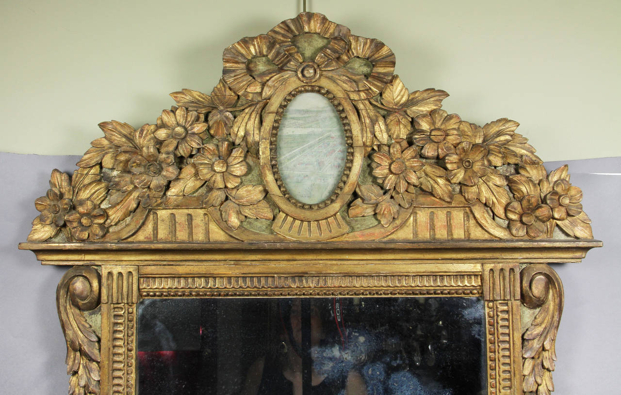 Arched carved crest with floral and leaf carving with central faded watercolor panel over a mirror plate set in a carved frame.