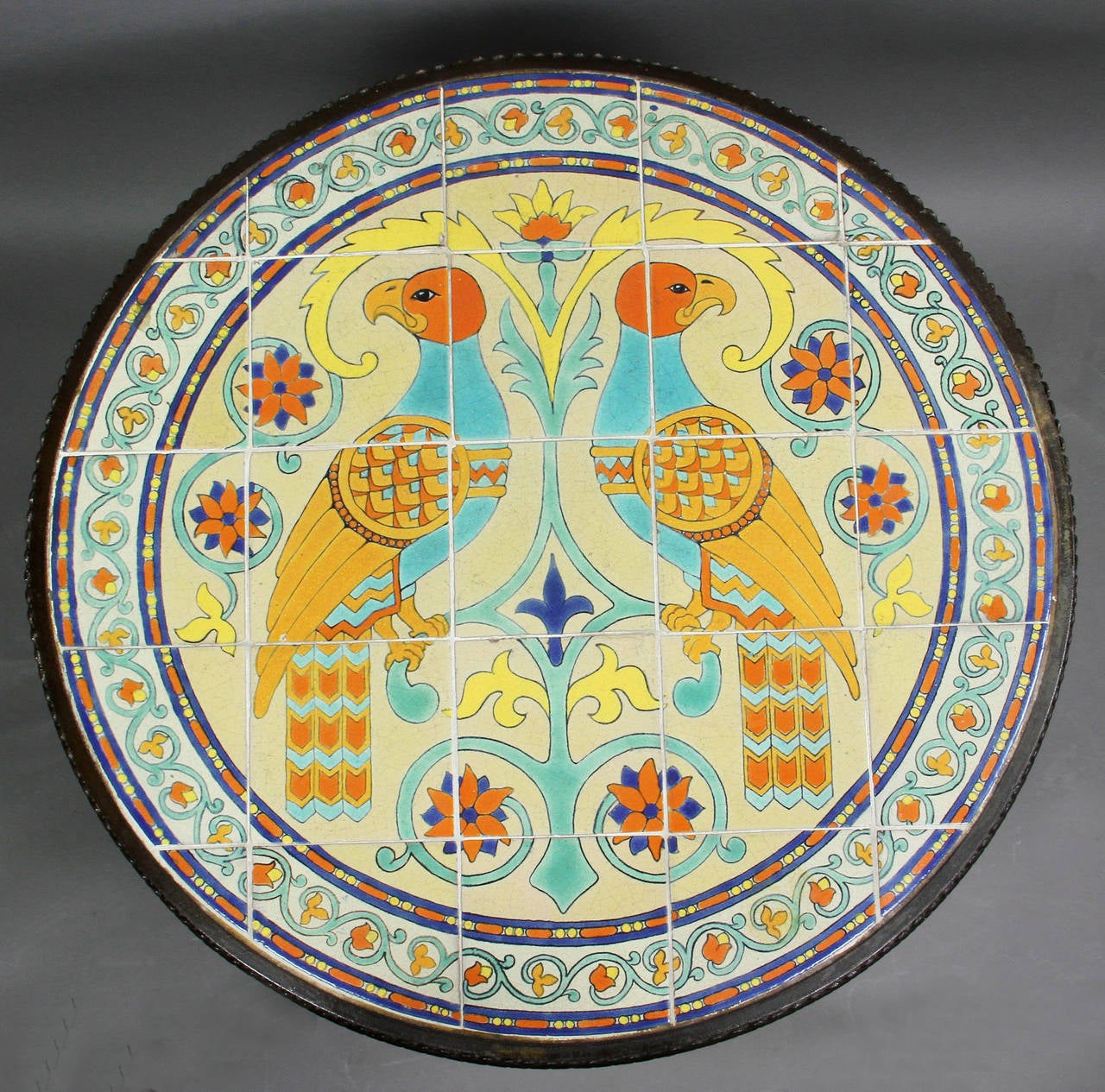 Circular top with 25 tiles with central pair of parrots, scrolls and flowers and vine and leaf border, serrated wrought iron edge to top, twist turned base, three twist legs with paw feet.