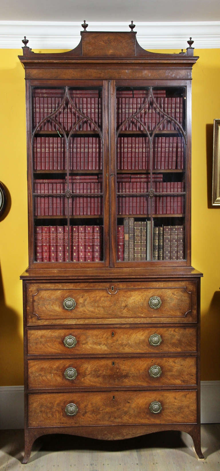 Arched tablet cornice with finials over two Gothic mullioned doors enclosing three shelves, the base with fold down drawer opening to a finely fitted interior over three graduated drawers, splayed leg base. Provenance; Sir Leon Bagrit , British