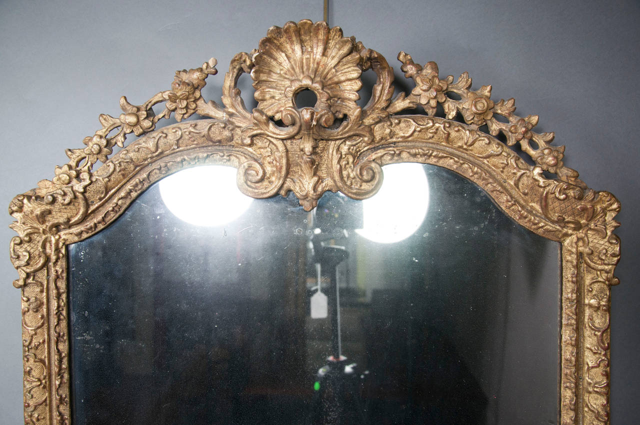 With central shell form crest flanked by floral and leaf carving, the frame with overall diaper pattern with scrolls, shells etc. Original gilded frame and mirror plate.