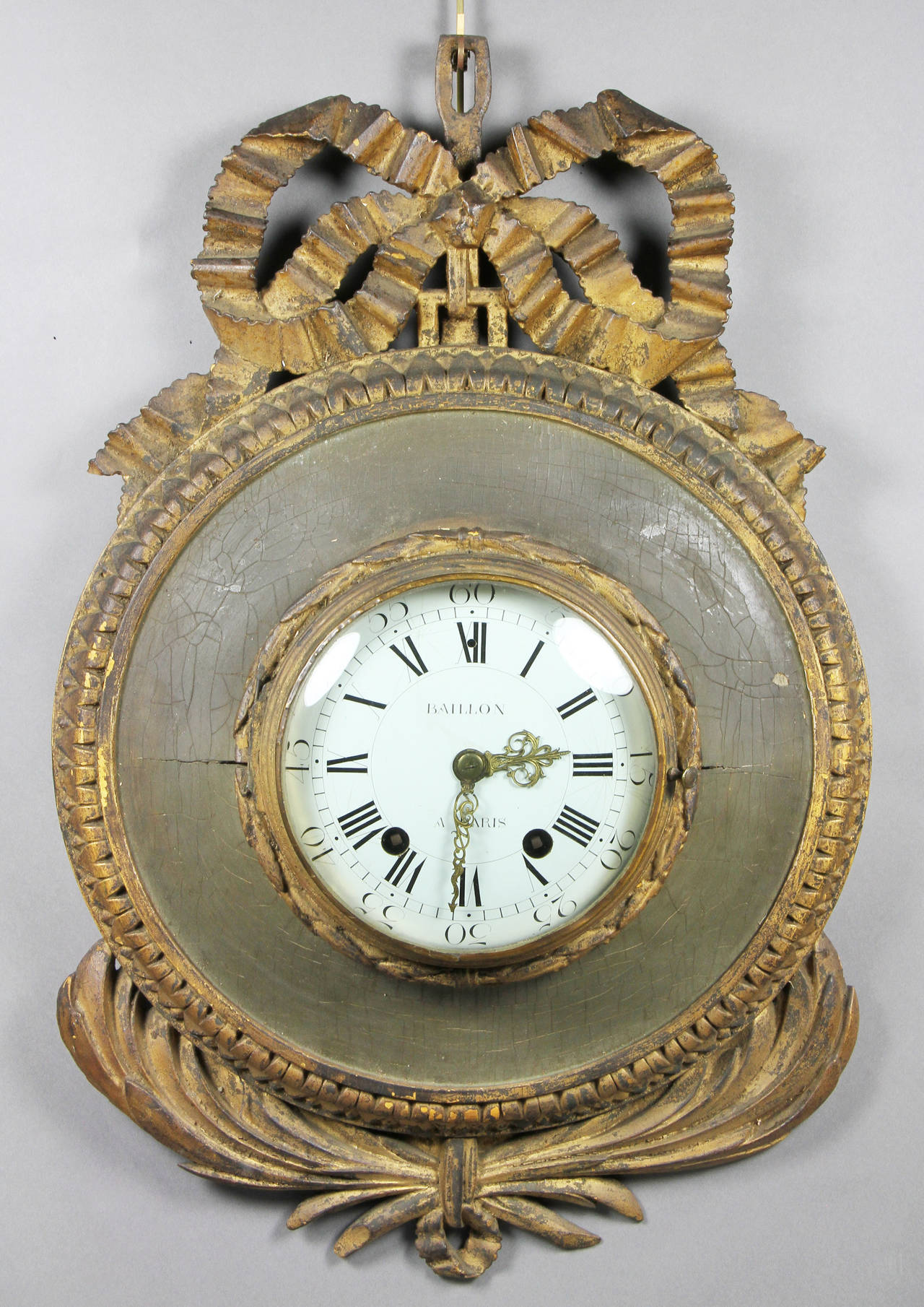 Circular enamelled clock dial signed and by Baillon  Paris , with a hinged domed glass door set in a circular wood case with carved ribbon crest and bundled olive leaves.