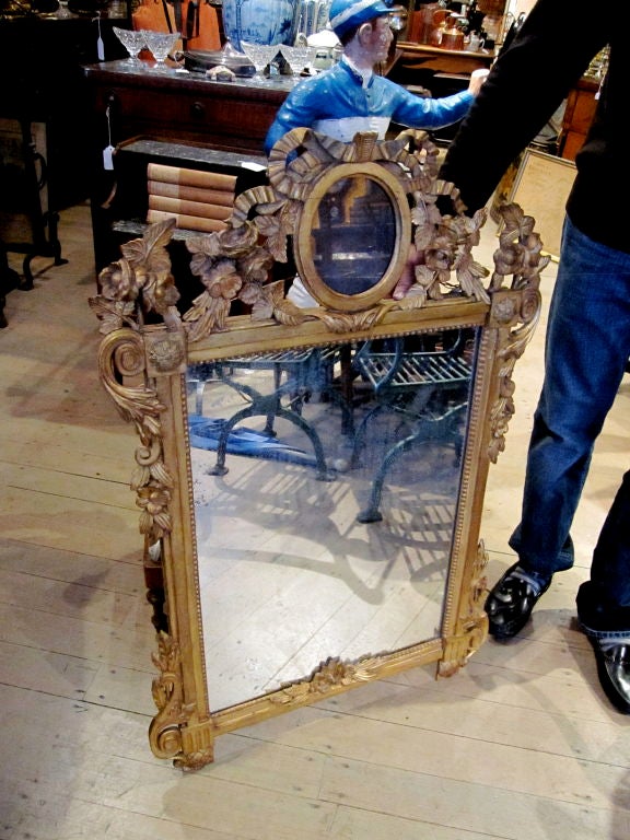 The arched arched top with central oval mirror and ribbon and flowerhead carving over a mirror plate within a carved frame.