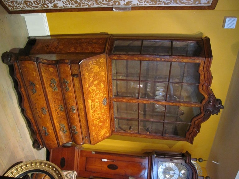 Arched carved cornice over a pair of glazed doors and also glazed on top sides, the base elaborately inlaid with a fold down writing lid enclosing a fitted interoir over three graduated drawers,claw feet. Bombe form