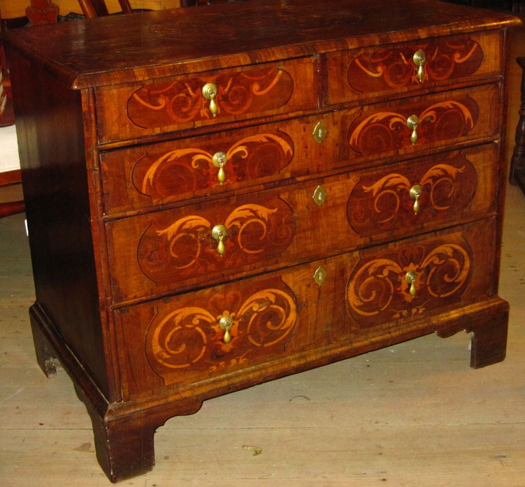 Rectangular top with central oval inlay with various woods including boxwood and rosewood, corner similarly inlaid, with cross banded edge, over two short drawers and three graduated long drawers, bracket feet.
